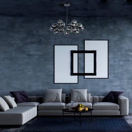 A modern living room features a gray sectional sofa with assorted pillows, a geometric art piece on a textured blue wall, and the Dallas 25 Light Suspension in chrome with smoky glass above a black coffee table holding a fruit bowl, all situated on a dark rug.