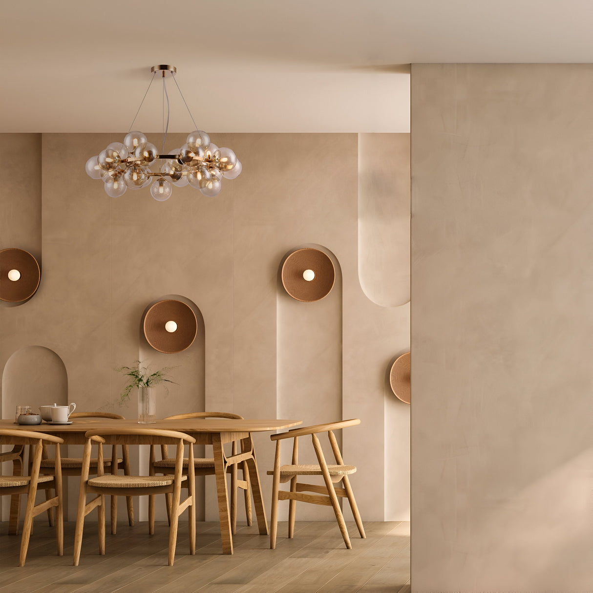 A minimalist dining room with a wooden table and chairs, teapot, and vase of flowers. Beige textured walls feature round recessed lights. A Dallas 25 Light Suspension - Gold With Amber Glass hangs elegantly above the table with spherical bulbs in a golden metal frame.