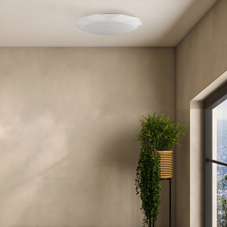 A minimalistic room boasts the Crystallize LED Flush Ceiling Light - White with dimmable settings. A vibrant green plant in a striped pot by a large window partially reveals the cityscape, contrasting with the rooms neutral walls.