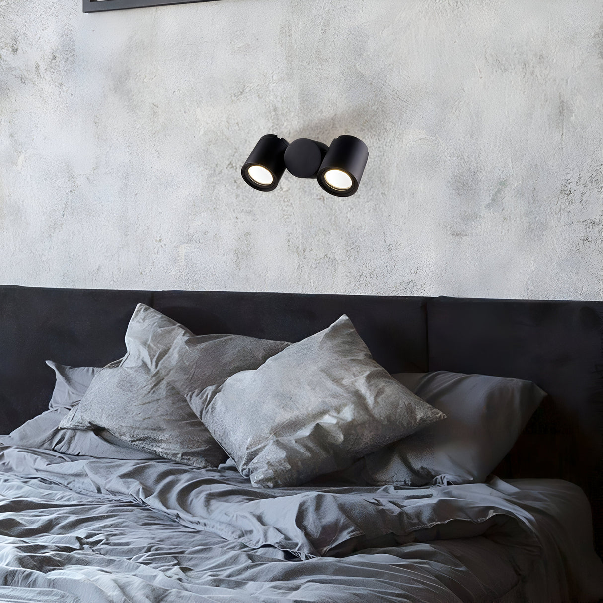 A modern bedroom highlights minimalist design with a gray textured wall, the sleek black Wall Street Outdoor Wall Light, and neatly arranged gray bedding. The monochromatic color scheme adds to the serene ambiance, capturing the elegance of minimalist style.