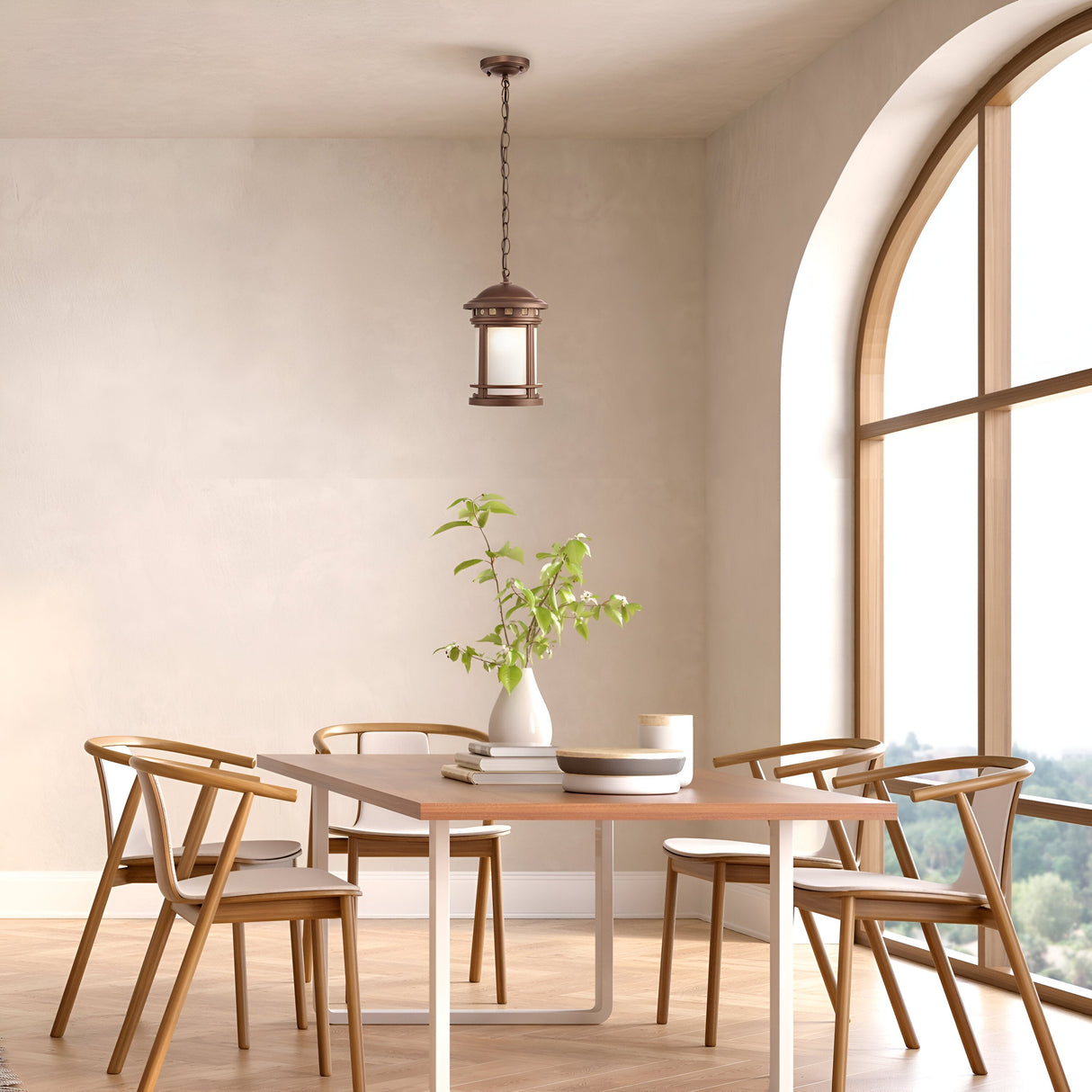 A modern dining room features a wooden table with five matching chairs, highlighted by the Salamanca Outdoor Pendant Light - Brown. A white vase with green foliage adorns the table, large arched windows bathe the space in natural light, and neutral-colored walls add to its elegance.