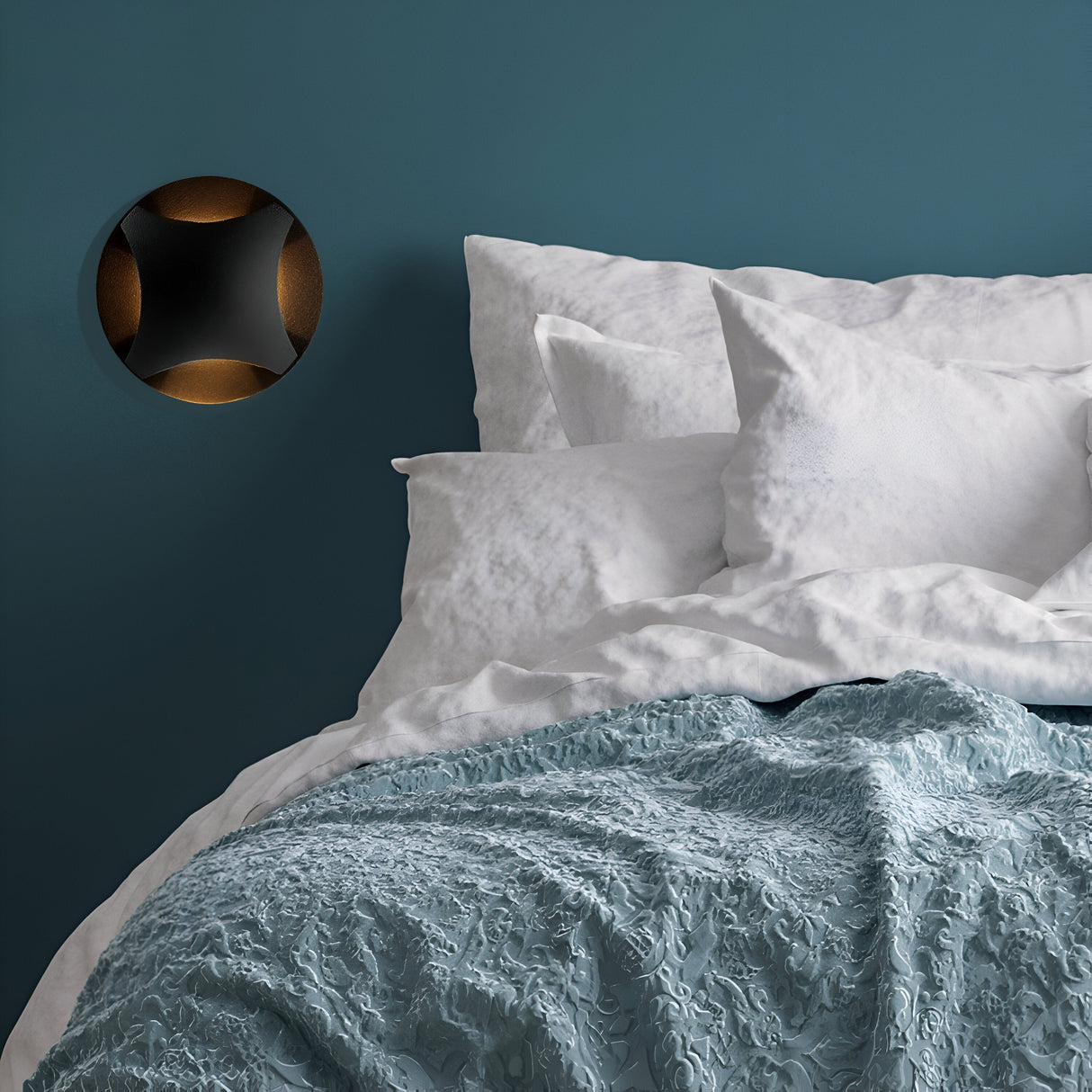 A neatly made bed with white pillows and a textured light blue blanket is set against a teal wall, featuring the Biscotti Outdoor 4 Beams LED Recessed Wall Light in Black, emitting a warm amber glow.