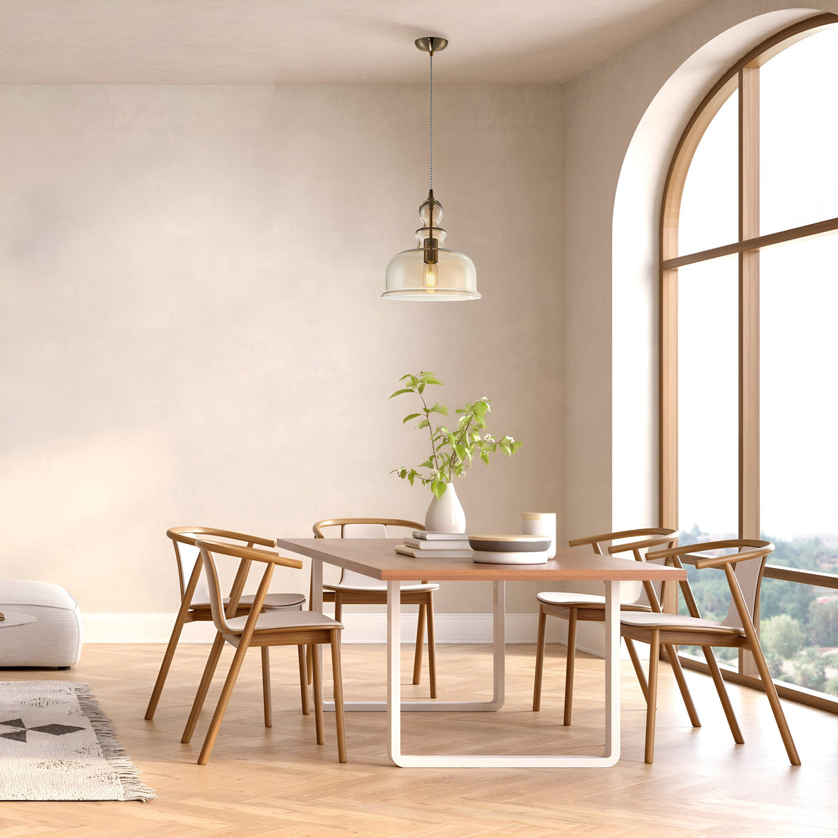 A modern dining room with a wooden table and four matching chairs exudes vintage charm. A plant in a vase sits beneath the Tone Pendant Light - Bronze With Amber Half Dome Glass. The large arched window, beige walls, and wood flooring create a bright and airy atmosphere.