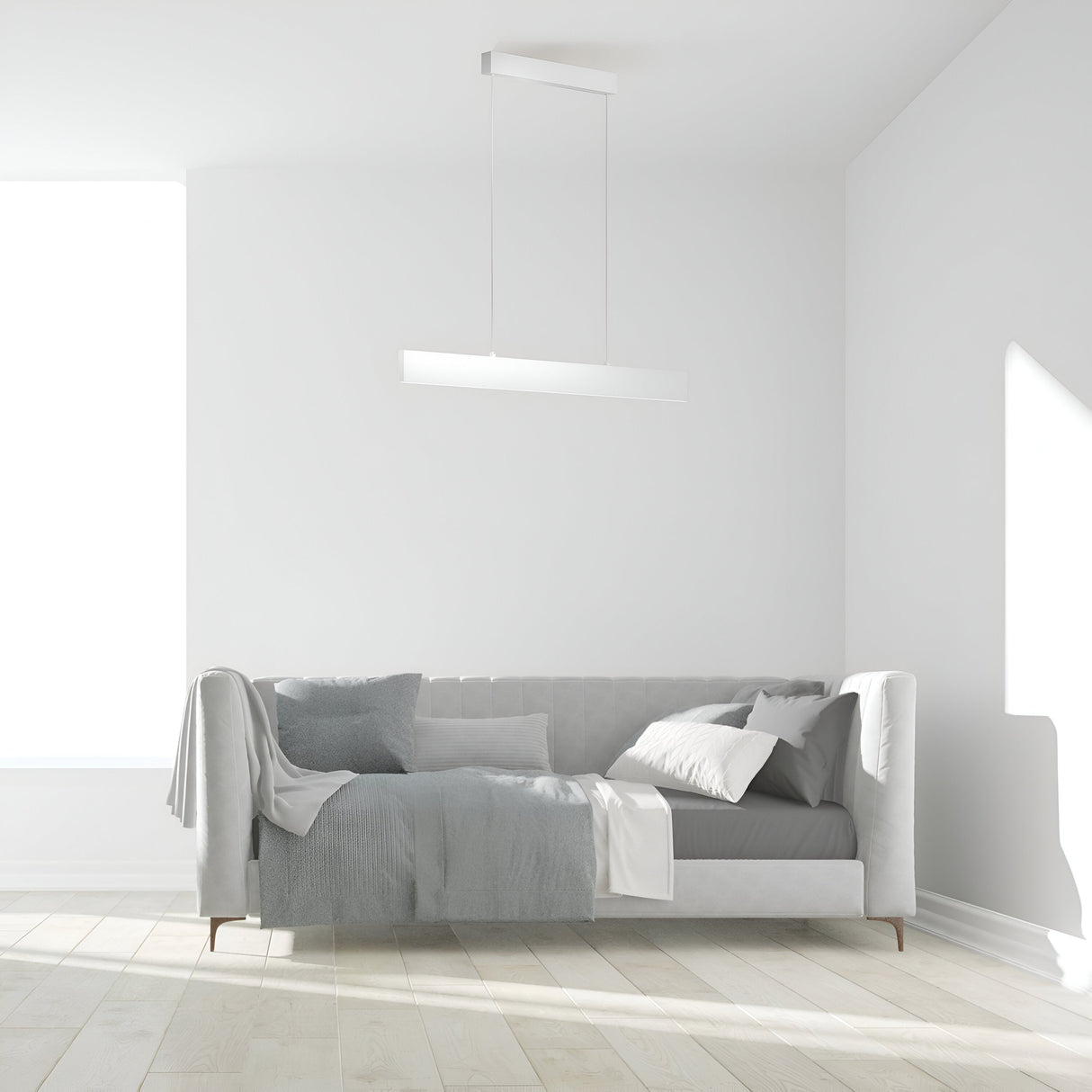 In a minimalist living room, a sleek gray sofa with pillows and a throw sits against a white wall. The Step LED Linear Suspension Light 4000K 23W in white offers energy-efficient lighting, while sunlight through a large window highlights the natural glow of the light wood floor.