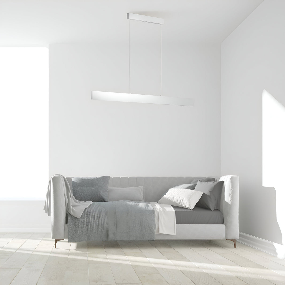 A minimalist living room includes a light gray sofa with cushions and a blanket. The Step LED Long Linear Suspension Light 4000K 30W - White adds modern flair, while natural light from a large window illuminates the light wooden floor, keeping the room bright.