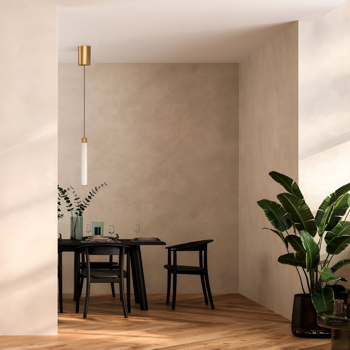 A minimalist dining area features a black table and chairs against beige walls. The Ray LED Short Pendant Light in gold and white hangs elegantly overhead. The table is adorned with glassware and a plant centerpiece, while potted plants decorate the chevron-patterned wooden floor.