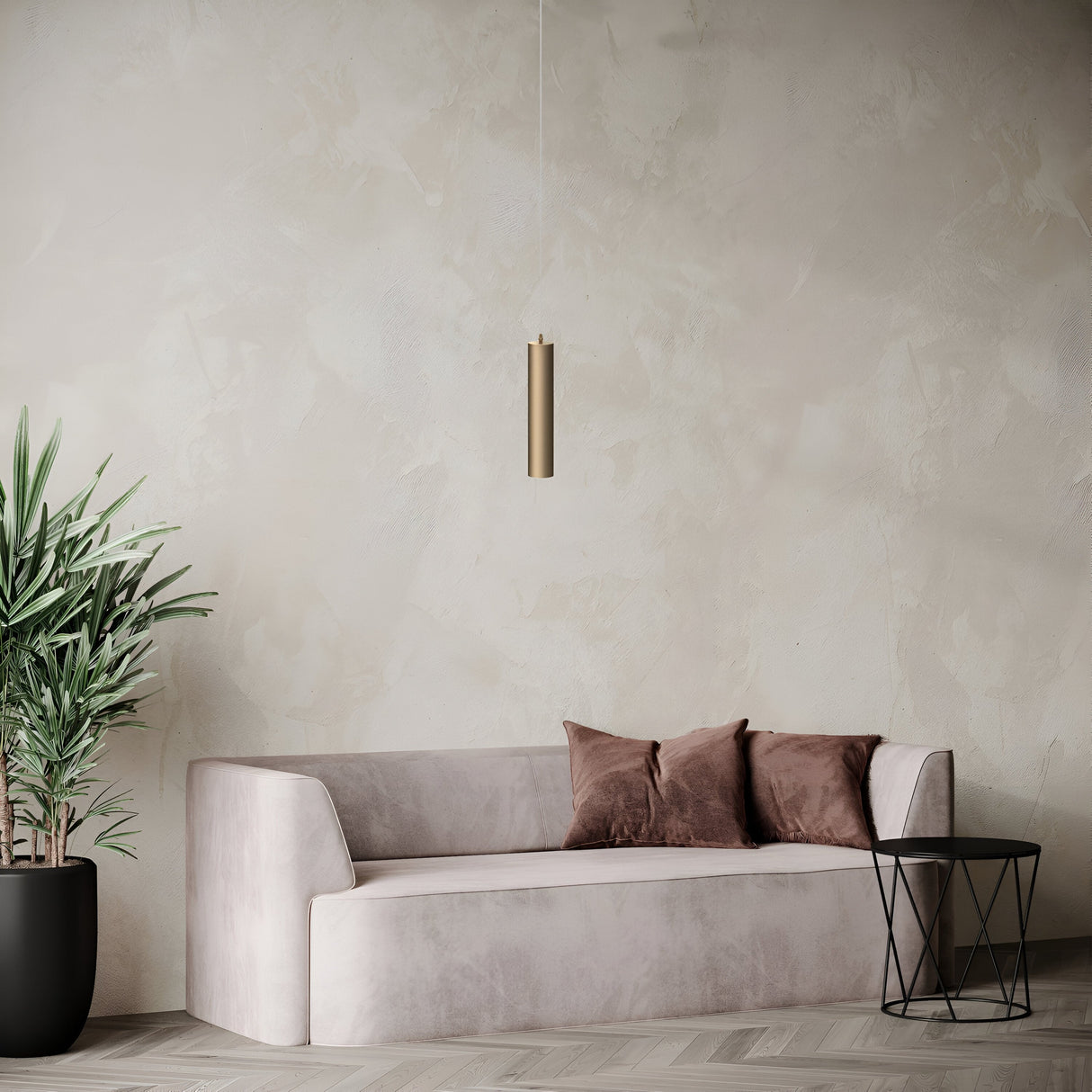 A minimalist living room showcases a beige sofa with two brown cushions, a small geometric black metal side table, and the Focus Single Pendant Light in matte gold. The textured neutral wall and herringbone hardwood floor pair with a potted plant for added greenery.