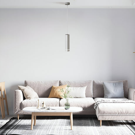 A modern living room features a light gray sofa with pastel cushions and a minimalist coffee table adorned with decor items. The Orlo LED Pendant Light 4000K in white hangs above, while a patterned rug complements the neutral palette, enhancing the interiors modern feel.