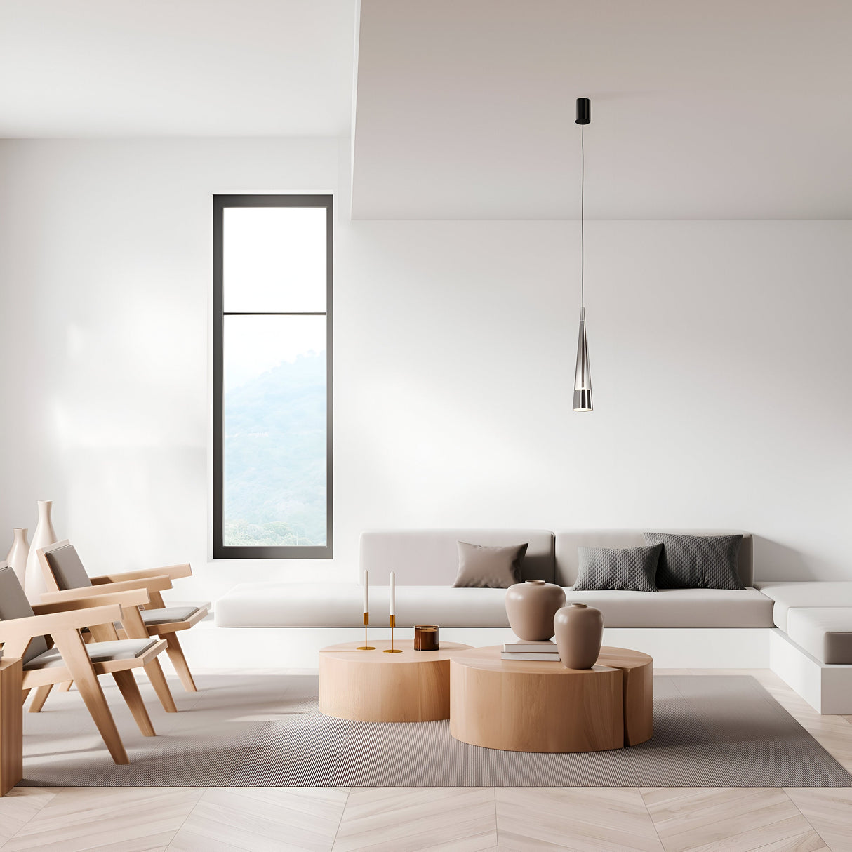 A minimalist living room features light gray and wooden tones with a low, modern sofa and round wooden coffee tables adorned with vases. Wooden chairs complement a tall narrow window, while a Sintesi 1 Light LED Pendant in chrome adds contemporary lighting from above.