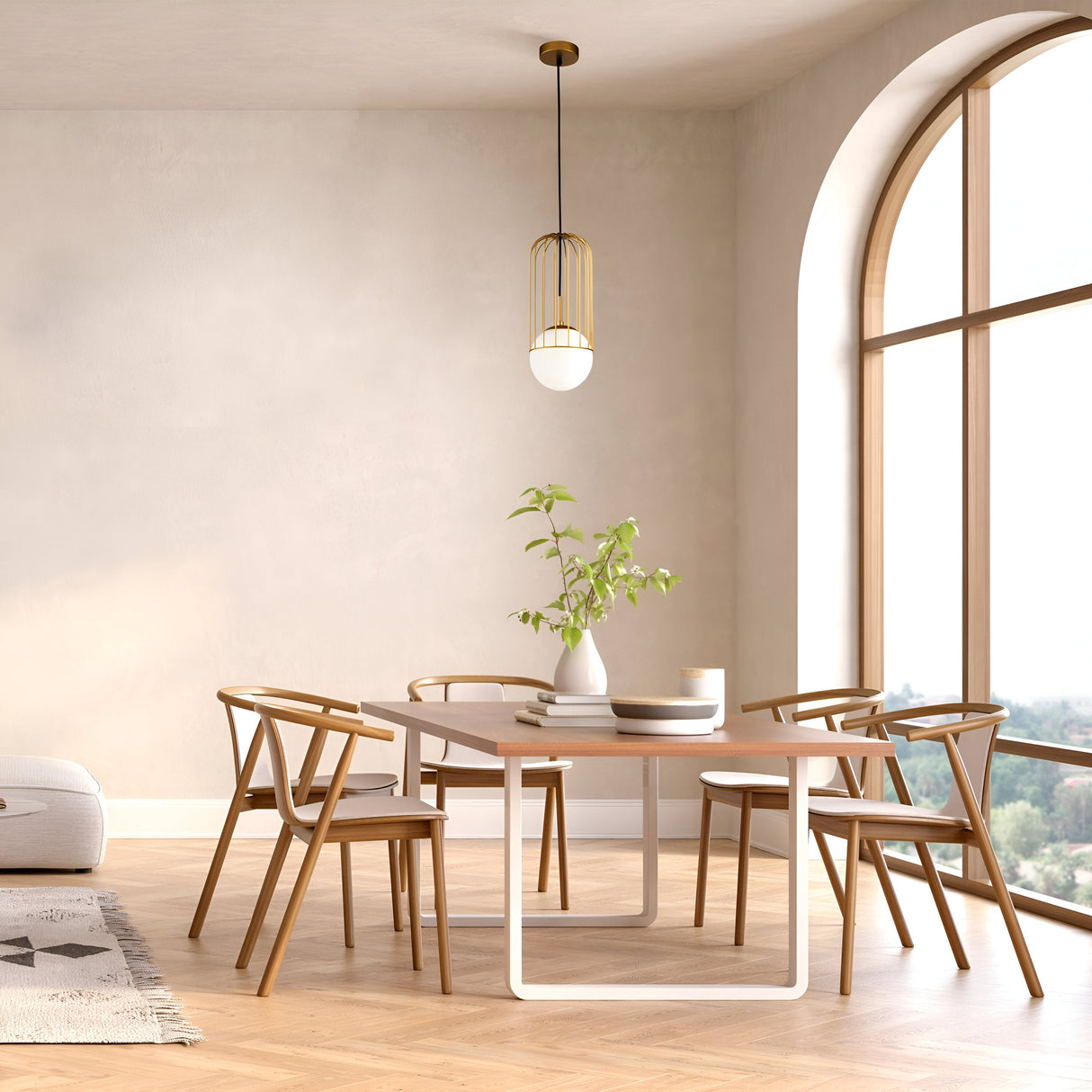 A modern dining room features a wooden table with five matching chairs, a white vase with green branches, and the Telford Pendant Light in gold and medium white glass above. Large arched windows let in natural light, illuminating the wooden floor and soft-toned walls.