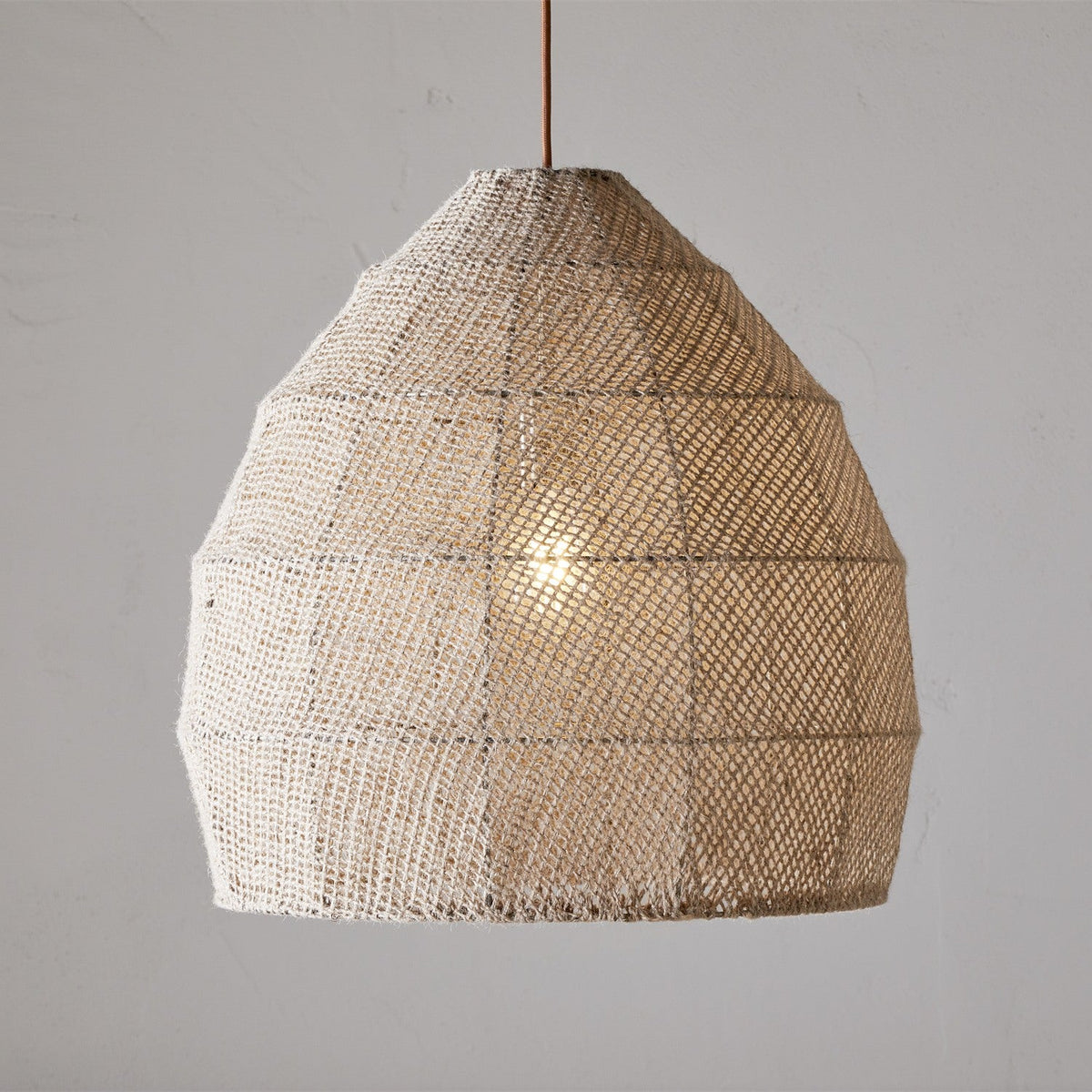 Jahari Woven Jute Pendant Light in natural tones, large dome-shaped open weave shade with visible seams and rust-coloured cord, lit bulb visible through mesh against a plain grey background.