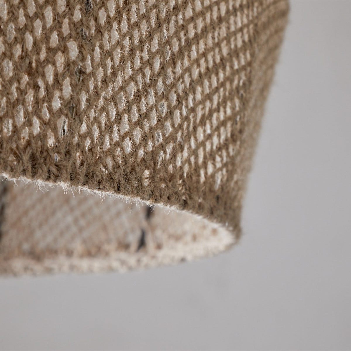 Close-up of the Jahari Woven Jute Pendant Light in natural, showing the coarse open-knit jute weave and raw rim edge against a plain light grey background.