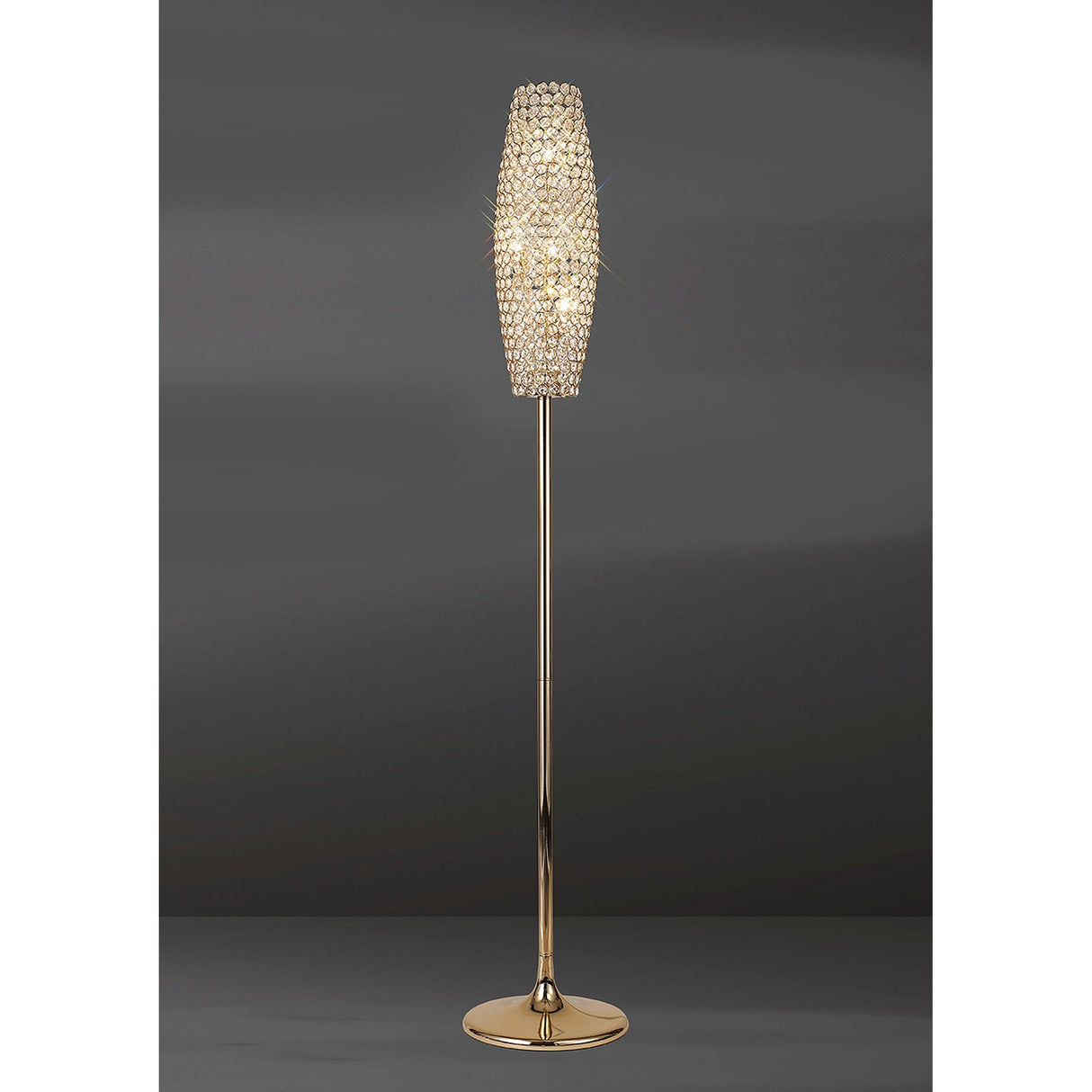 The Kos 4 Light Crystal Floor Lamp in French Gold features a slim stand and a tall, oval crystal-accented shade, glowing brilliantly against a dark gray backdrop.
