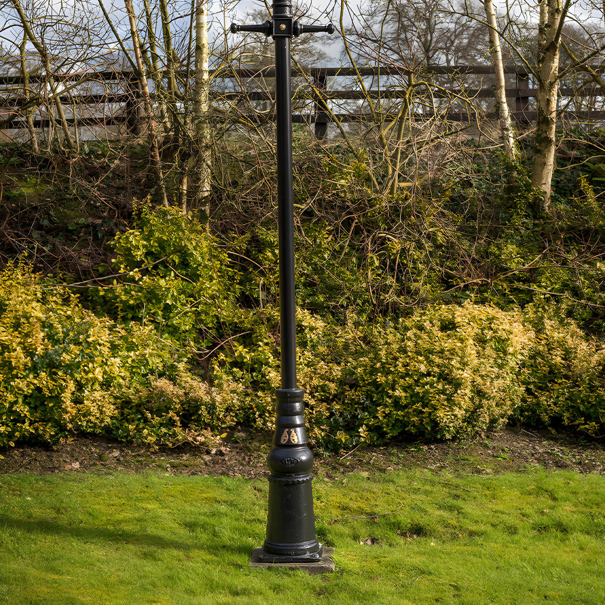 Victorian Cast Iron Lamp Post Column, 2.36m black metal pole with decorative base and cross-arm top, set on grass before hedges and trees in a garden setting.