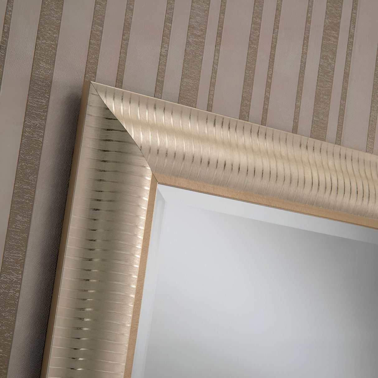 This close-up showcases a corner of the Veris Rectangle Wall Mirror in Champagne, featuring a ribbed texture that enhances its modern elegance. The beige wallpaper with vertical stripes in the background further complements its sophisticated design.