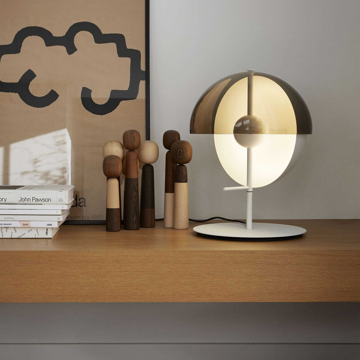 The Lucia LED Table Lamp - White sits on a wooden shelf among figurines and books, providing energy-efficient light and adding a modern touch to the space.