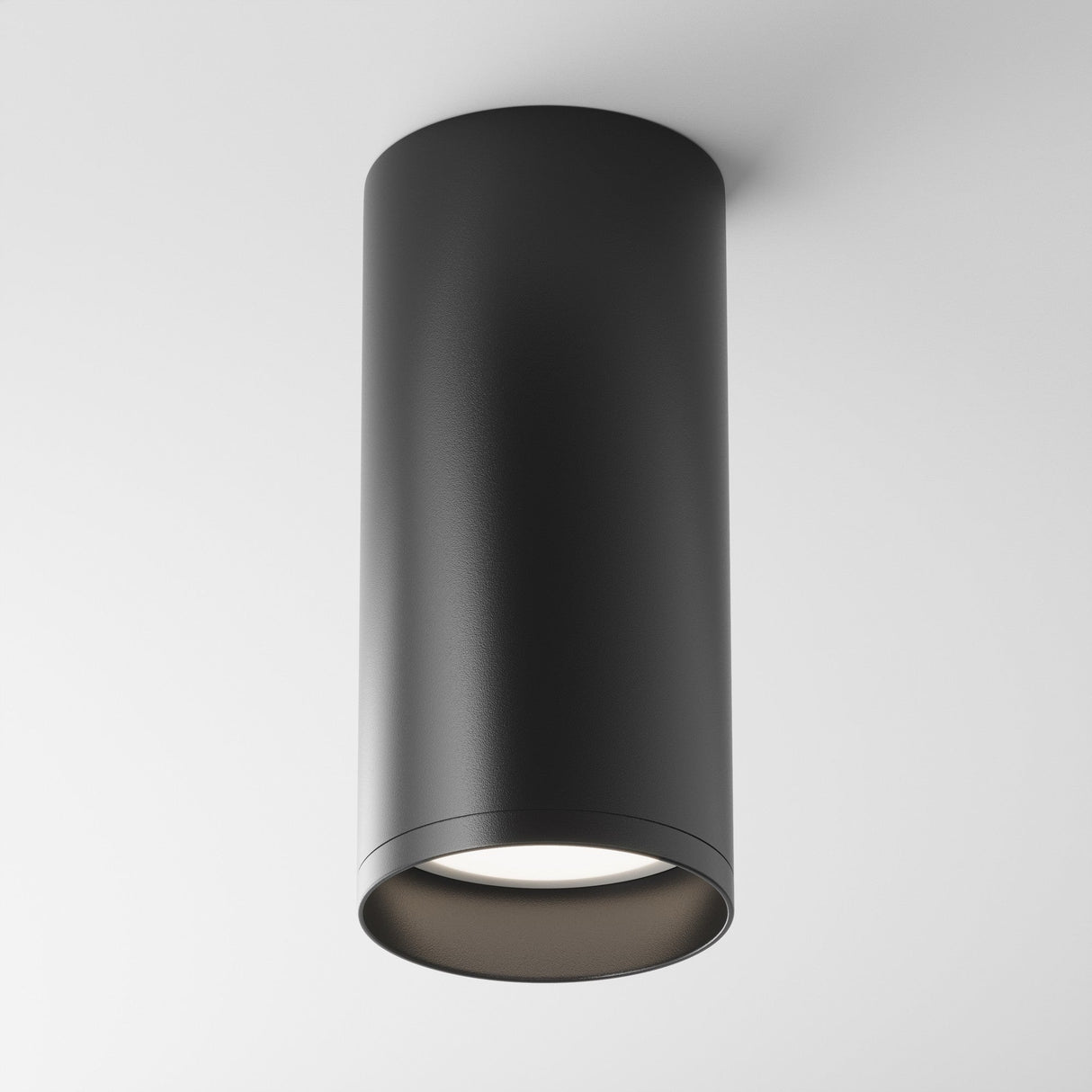 The Focus Fixed Round Surface Mounted Downlight in black features a modern cylindrical design, seamlessly attaching to a white ceiling. Its sleek, minimalist style embodies contemporary aesthetics, making it an ideal choice for modern lighting solutions.