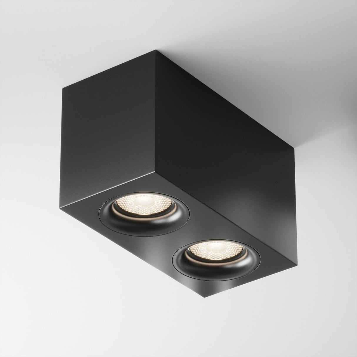 The Slim Twin Flat Rectangular Surface Downlight - Black is a modern industrial fixture with two circular recessed spotlights. Its sleek black aluminum design elegantly contrasts with the white ceiling, providing focused illumination.