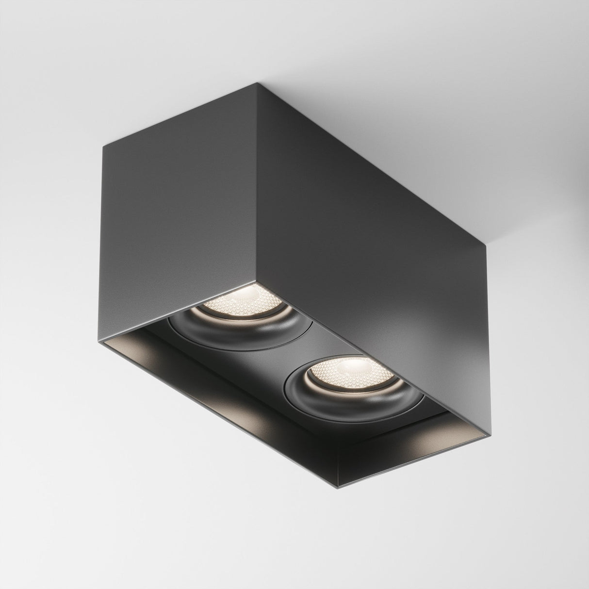 The Slim Twin Rectangular Surface Downlight - Black is a modern rectangular ceiling fixture with two recessed spotlights, featuring a matte black aluminium body that emphasizes clean lines and an industrial aesthetic on a white ceiling.