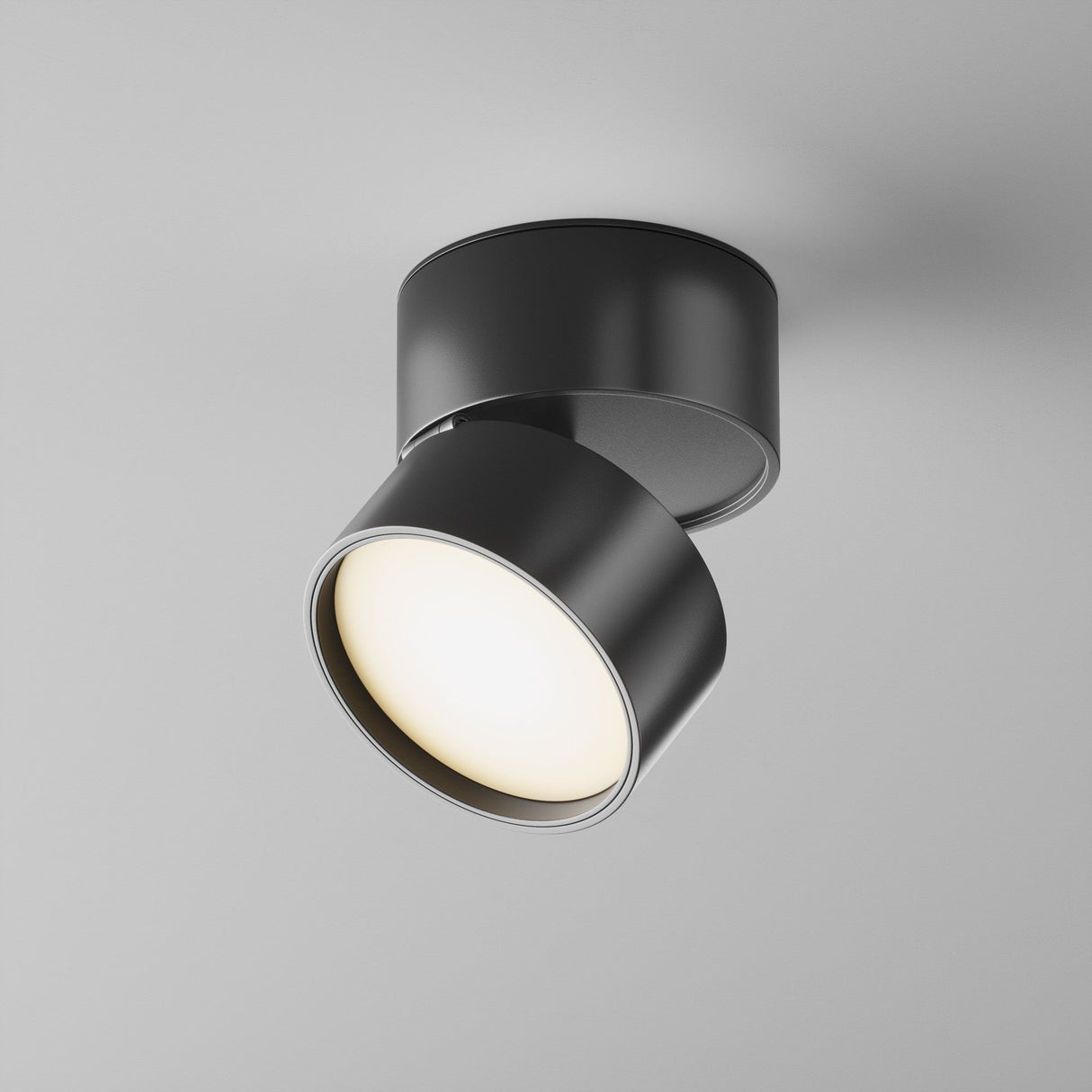 The Onda LED Single Spotlight 12W 3000K - Black is shown with its modern, round design angled to illuminate a surface. Its energy-efficient light is on, casting a soft glow against a plain gray background.