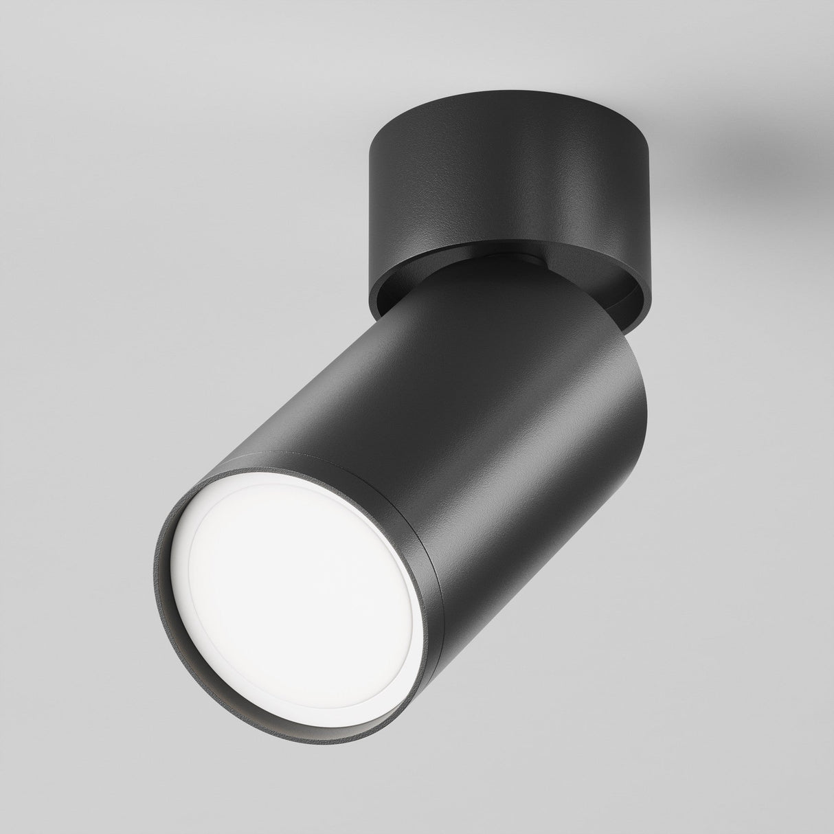 The Focus S Single Surface-Mounted Spotlight in black features a sleek, matte design angled downward to emit a soft glow. Its a contemporary lighting solution enhanced by a plain gray backdrop.