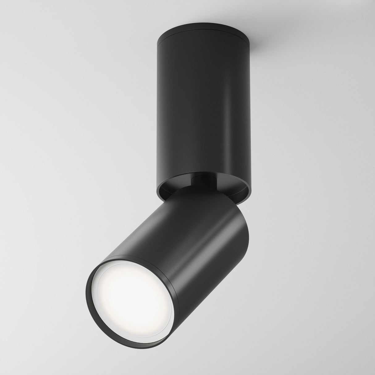The Focus S Long Single Surface-Mounted Spotlight in black offers a sleek, cylindrical design. Its adjustable and mounted on a white ceiling, angled downward to highlight its minimalist and modern style effectively.