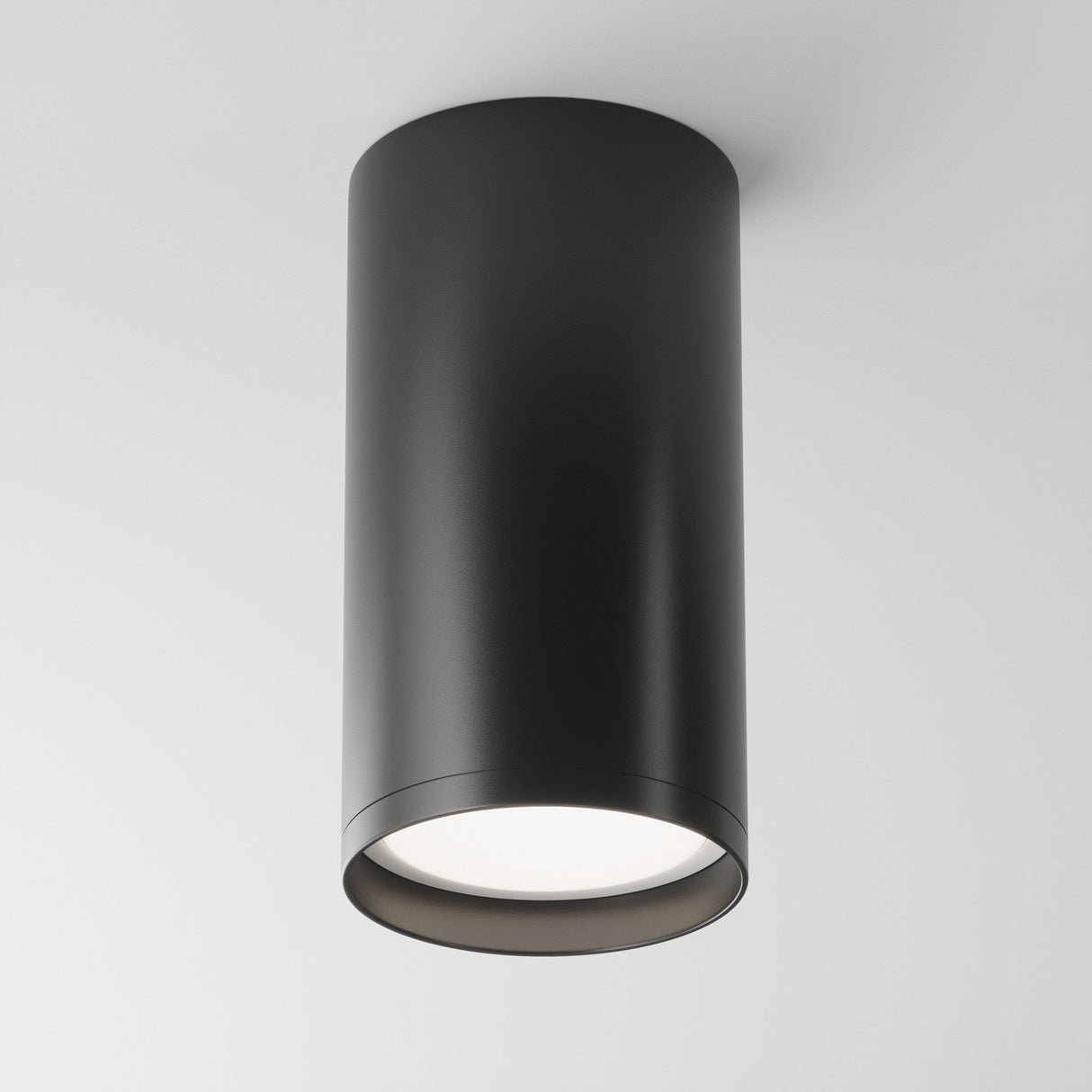 The Focus S Fixed Round Surface Mounted Downlight in black offers a modern industrial touch with its smooth cylindrical design. It emits soft white light downward and is perfect for a sleek addition to a white ceiling.