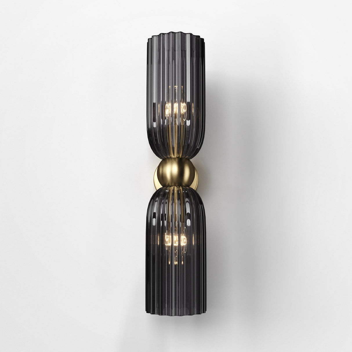 The Antic 2 Light Wall Light features two vertically aligned grey glass lampshades with a dark tint, separated by a central spherical brass accent. Embracing retro trends, it emits a warm glow from multiple bulbs on a white background.