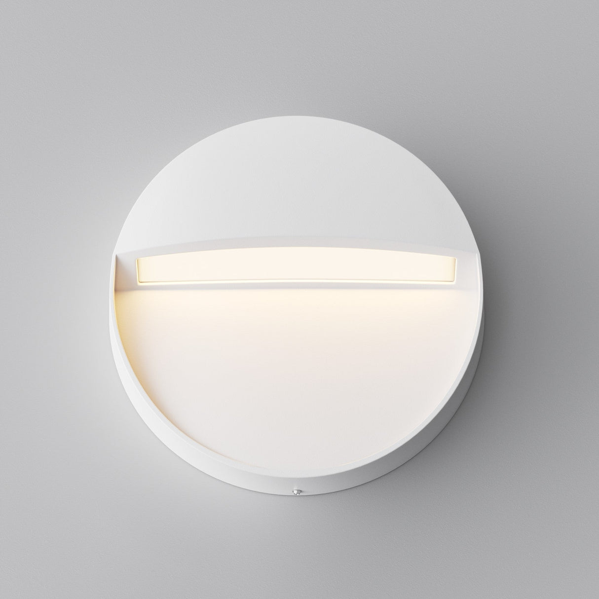 The Mane Outdoor LED Round Wall Light in white boasts a minimalist, circular design. Its energy-efficient LED lights cast a soft glow upwards and illuminate downwards, complementing modern aesthetics perfectly against a light gray background.