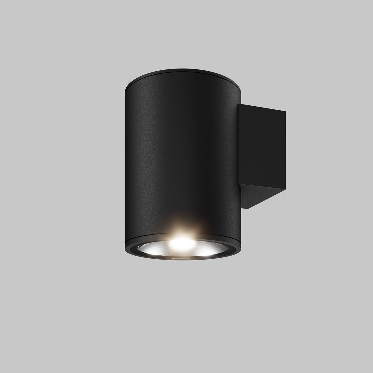 The Shim Outdoor Wall Light 5W 3000K in Graphite, featuring a black cylindrical design and IP65 rating, is wall-mounted against a plain gray backdrop. The illuminated LED bulb casts a gentle glow downward.