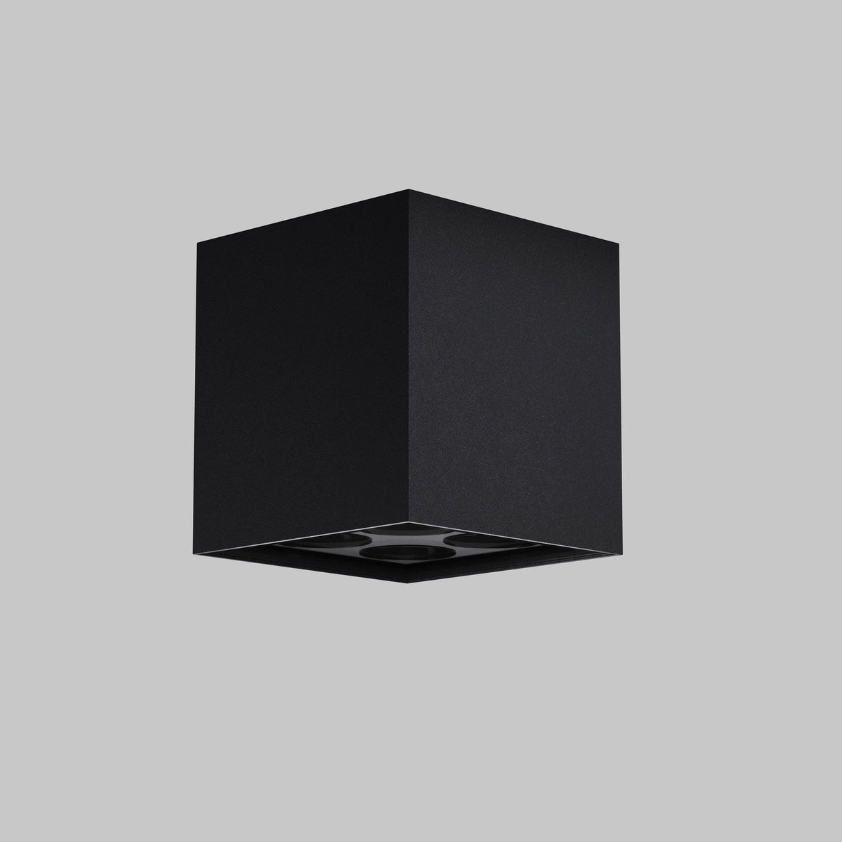 The Ares Outdoor LED Square Downlight in graphite, an energy-efficient, minimalist black cubic fixture with a recessed light, subtly enhances any gray backdrop with its sleek elegance.