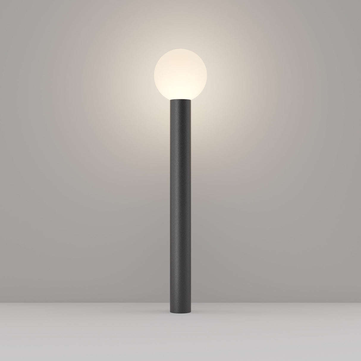 The Bold Bollard Light 80cm - Black boasts a sleek, dark aluminium cylindrical base and a glowing white spherical bulb, resembling an elegant bollard light. It presents beautifully against a plain grey background.