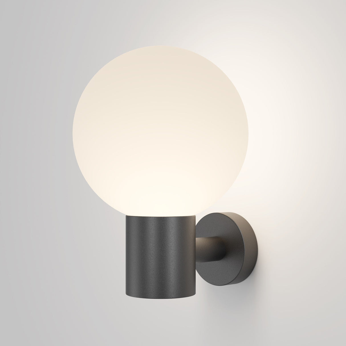 The Bold Outdoor Wall Light - Black (O598WL-01B) is a minimalist IP65-rated wall sconce with a round frosted glass globe on a sleek, cylindrical black metal mount. It emits a soft, warm glow, creating a cozy ambiance on light-colored walls. Ideal for both indoor and outdoor use.