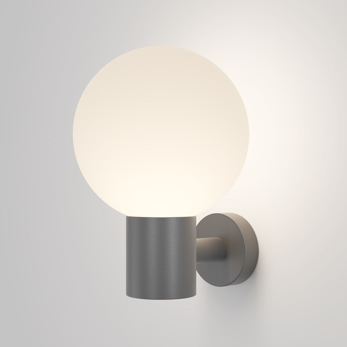 The Bold Outdoor Wall Light - Grey (O598WL-01GR) features a minimalist design with a round frosted glass shade for soft light and a simple cylindrical metal fixture with a matte finish, providing a modern touch to any plain, light-colored wall and offering subtle weather resistance.