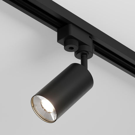 The Focus Mini Single Phase Unity Track Spotlight - Black is a modern black track light with a sleek cylindrical shape mounted on a ceiling rail. It emits bright, focused downward light, perfect for modern industrial interiors and stands out beautifully against a white background.