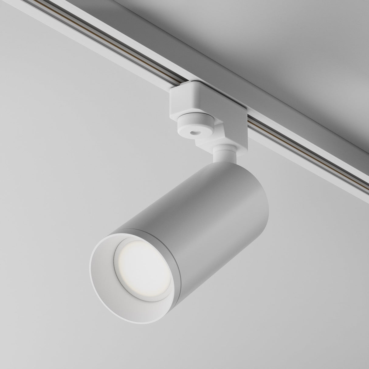 The Focus Single Phase Unity Track Spotlight in white is mounted on a ceiling rail, directing light downward. Its modern cylindrical design and swivel mechanism enhance its minimalist aesthetic, offering flexible illumination options.