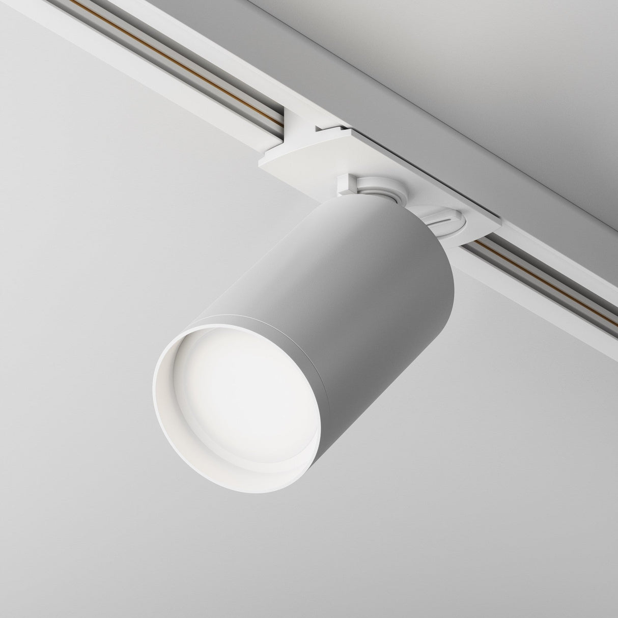The Focus S Single Phase Unity Track Spotlight in white is a cylindrical fixture mounted on a ceiling track, offering precision lighting control and adjustable directional lighting, casting a soft glow on the smooth, light-colored ceiling for a minimalist design.