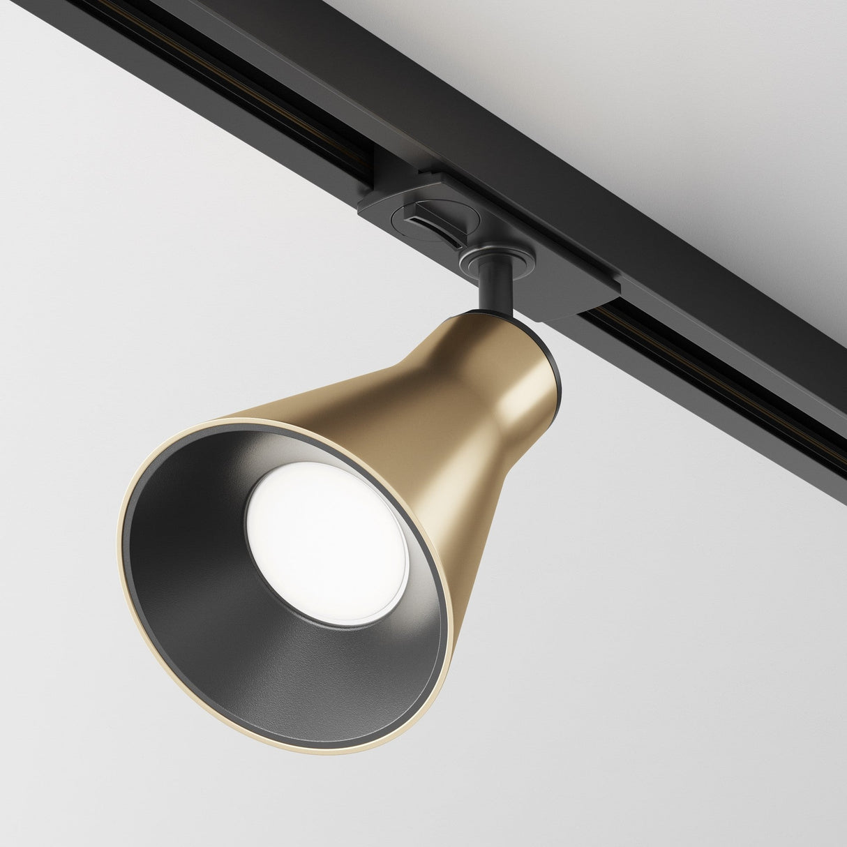 The Virar Single Phase Unity Track Spotlight in matte gold features a swivel mechanism and mounts on a black rail against a white ceiling. Its conical design directs light downward, offering sleek accent lighting with a minimalist aesthetic.
