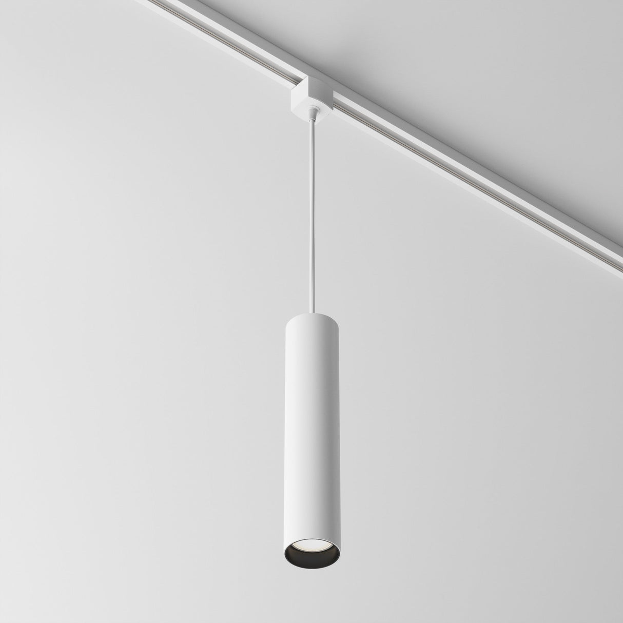 The Focus Single phase UNITY Track Pendant Light - White features a sleek, cylindrical design and hangs with an adjustable cable from a white ceiling to enhance the modern industrial aesthetic with its minimalist style.
