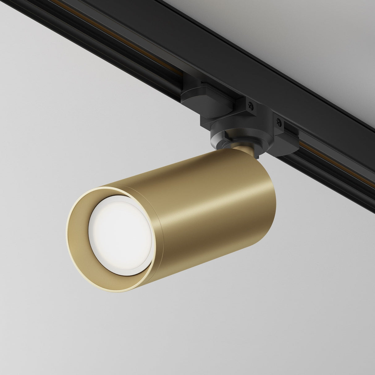 The Focus 3-Circuit Trinity Track Spotlight in matte gold features a sleek cylinder design on a black rail, ideal for enhancing industrial interiors with its modern appeal against a white backdrop.