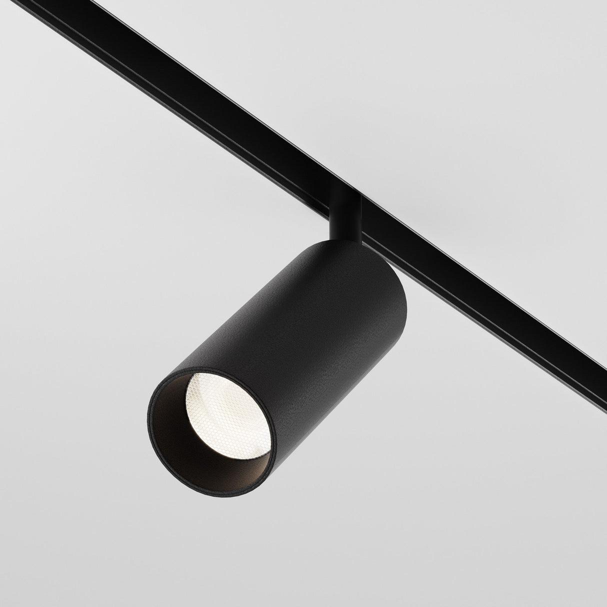 The Focus LED Magnetic Exility Track Spotlight 12W 4000K in black is mounted on a ceiling rail against a light gray background, emitting a soft glow that beautifully enhances modern interiors with its sleek and elegant design.