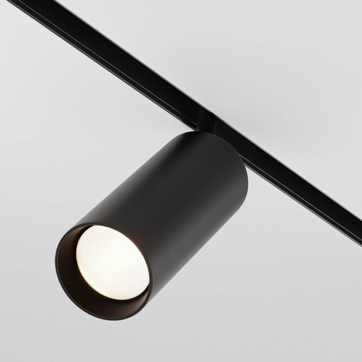 The black Focus LED Magnetic Exility Track Spotlight 20W 4000K, with a low-glare design, mounts on a ceiling rail emitting a soft white glow against a plain, light-colored ceiling background.