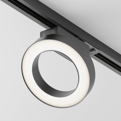 The Rim LED Single Phase Unity Track Spotlight, 12W in black, is a modern circular fixture with a black and white design. It mounts on the ceiling and emits neutral 4000K light from an adjustable edge contrasting with its black track spotlight body.