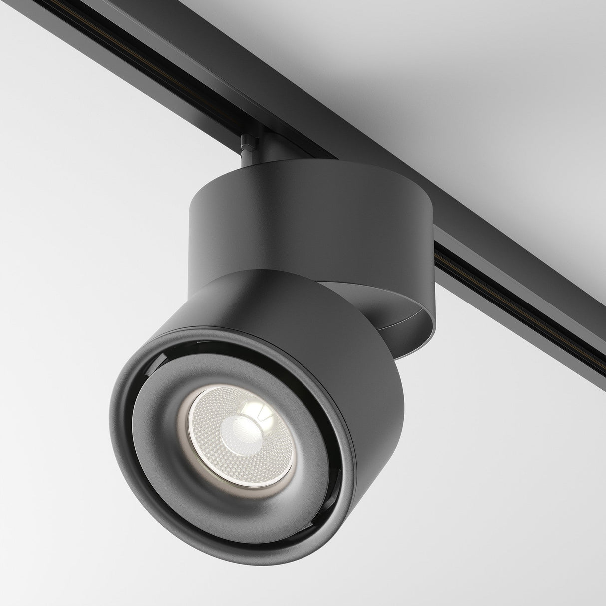The Yin LED Single Phase Unity Track Spotlight, in black with a 15W cylindrical design, is mounted on a ceiling rail. It emits a crisp 4000K light with a CRI of 90, projecting downward to create a modern look against the plain white ceiling.