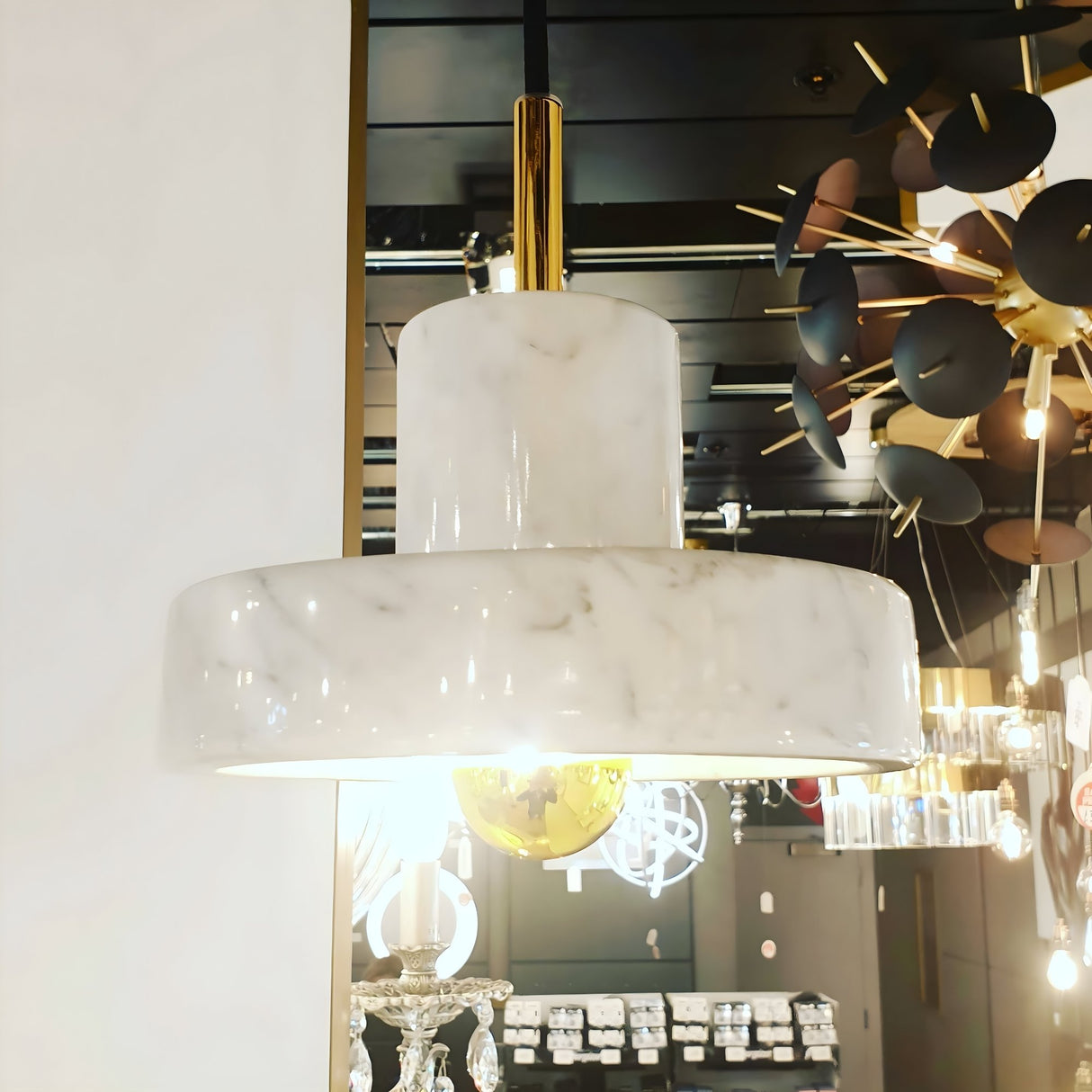 The Marble Pendant Light - White & Gold hangs in a showroom, displaying its modern design and gold accents alongside other contemporary lighting fixtures.