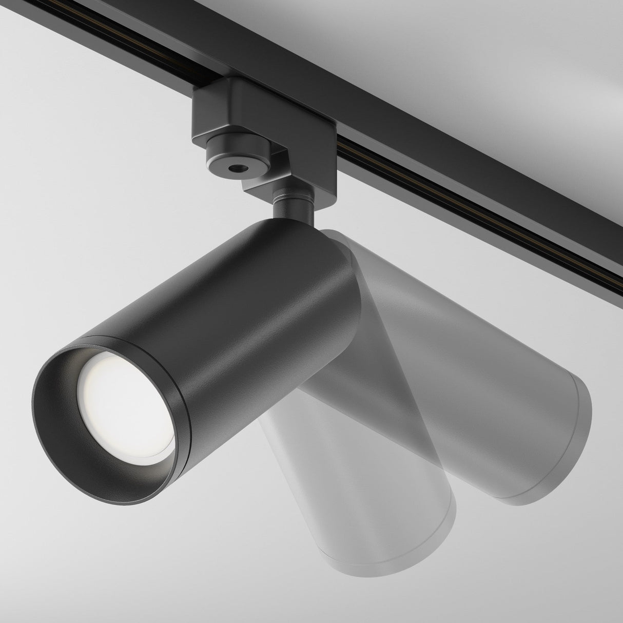 The Focus Single Phase Unity Track Spotlight - Black, with its cylindrical design, is affixed to the ceiling in overlapping positions to demonstrate adjustability and visual comfort. Its GU10 bulbs, switched on, cast a soft white glow against the light gray ceiling.