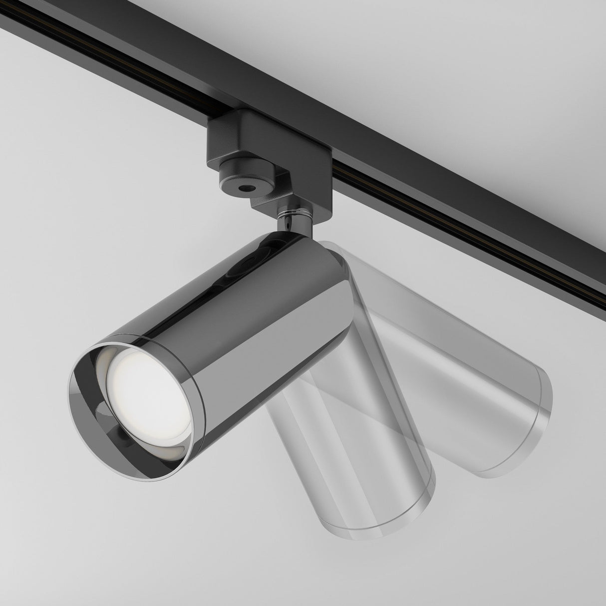 The Focus Single Phase Unity Track Spotlight in graphite, featuring a sleek chrome cylindrical design on a black track, is angled downwards against a gray ceiling, offering clean lines and reflective surfaces with GU10 bulb compatibility.