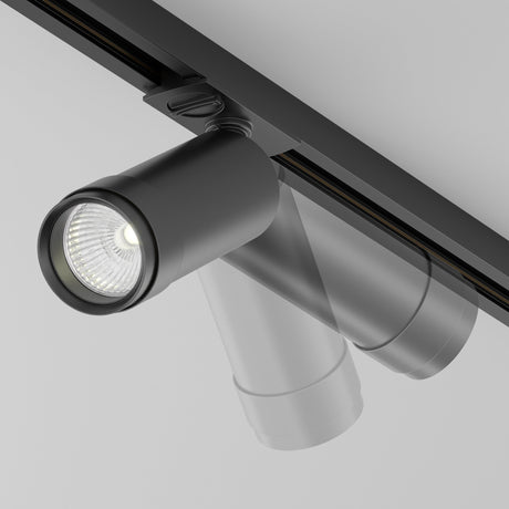 Close-up of the Focus Zoom LED Dimmable Single Phase Unity Track Spotlight 12W 4000K in black, mounted on a ceiling. The modern cylindrical light is angled downward, emitting bright white low-glare lighting. Both the fixture and ceiling boast a sleek, minimalist design.