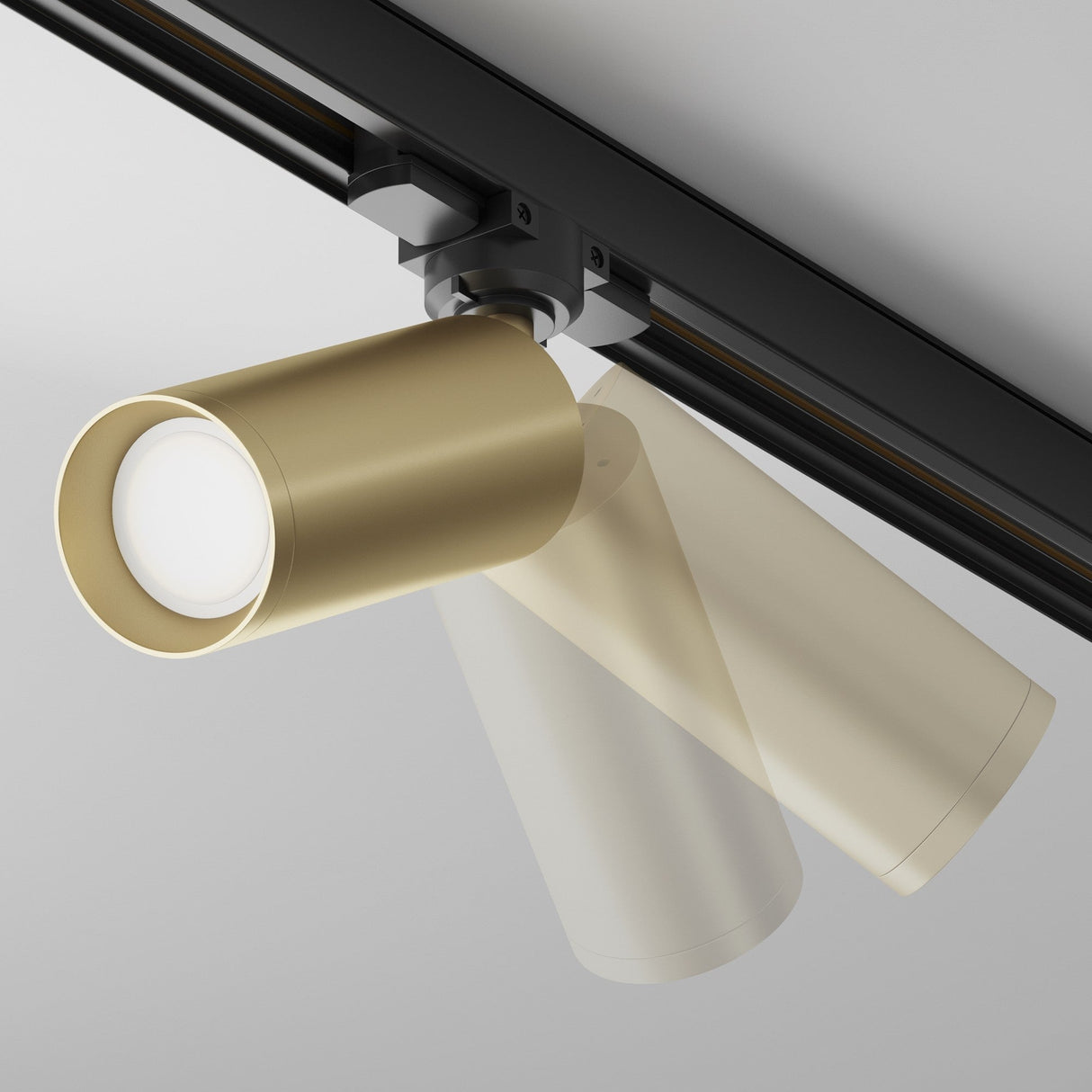 The Focus 3-Circuit Trinity Track Spotlight, in matte gold, is mounted on a black rail against a white ceiling. This cylindrical spotlight is ideal for industrial interiors, shown in three positions to demonstrate its adjustable swivel feature.