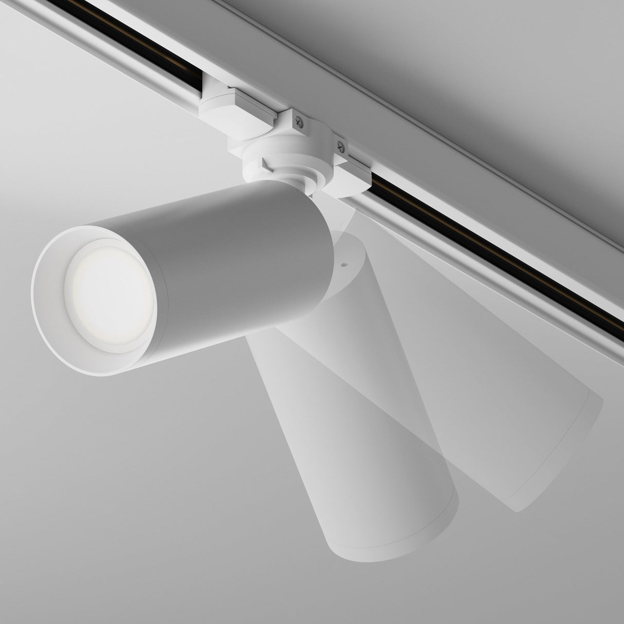 The Focus 3-Circuit Trinity Track Spotlight - White features a GU10 base and mounts on a ceiling rail. Its overlapping positions highlight its adjustable lighting, while the sleek design of both the ceiling and light emphasizes a modern aesthetic.